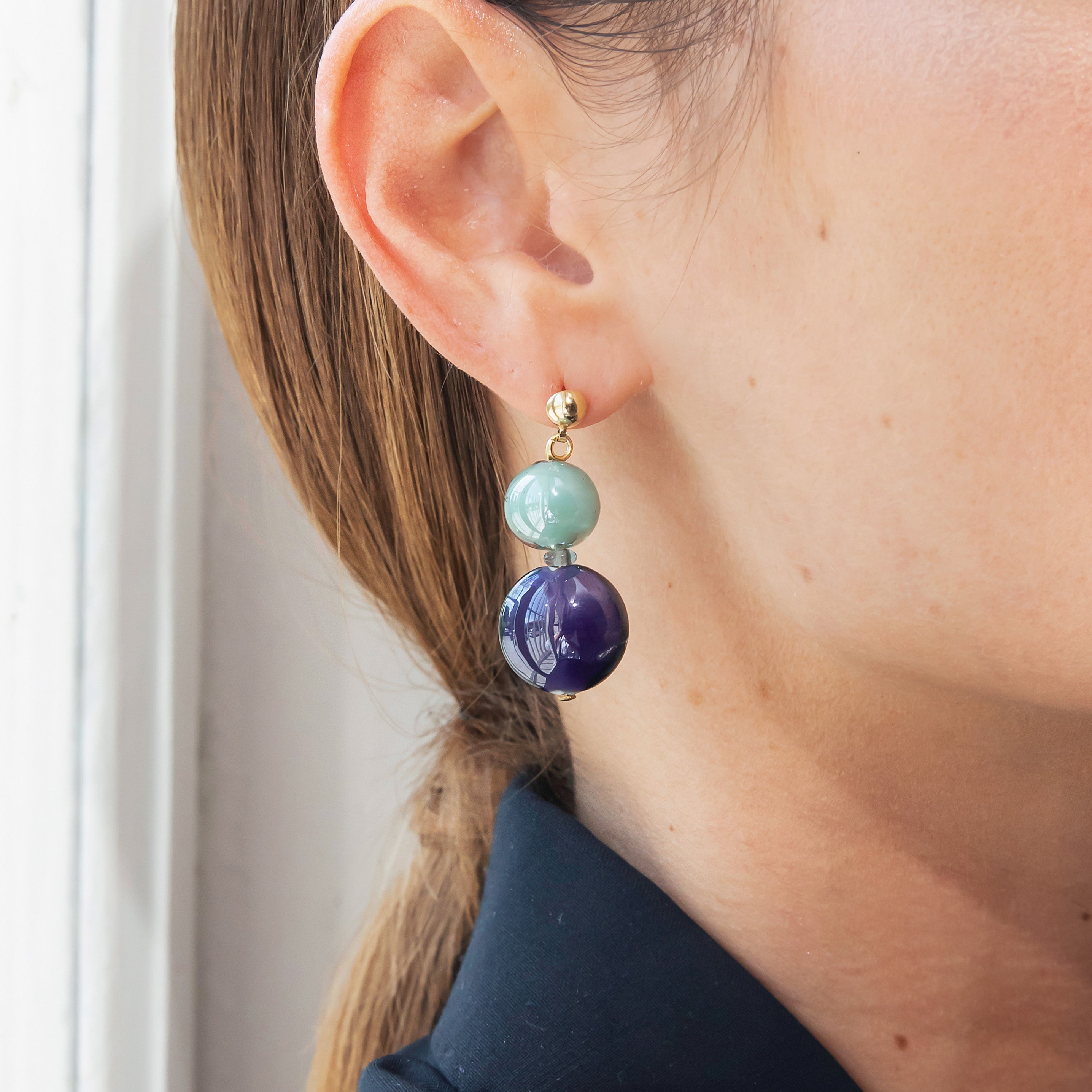 Model wearing MURRINAMURANO Venezia earrings from the Gaia Collection, handcrafted in Original Murano glass, 18KT Gold Finish or Rhodium finish, over Brass. Made in Italy – murrinamurano.us