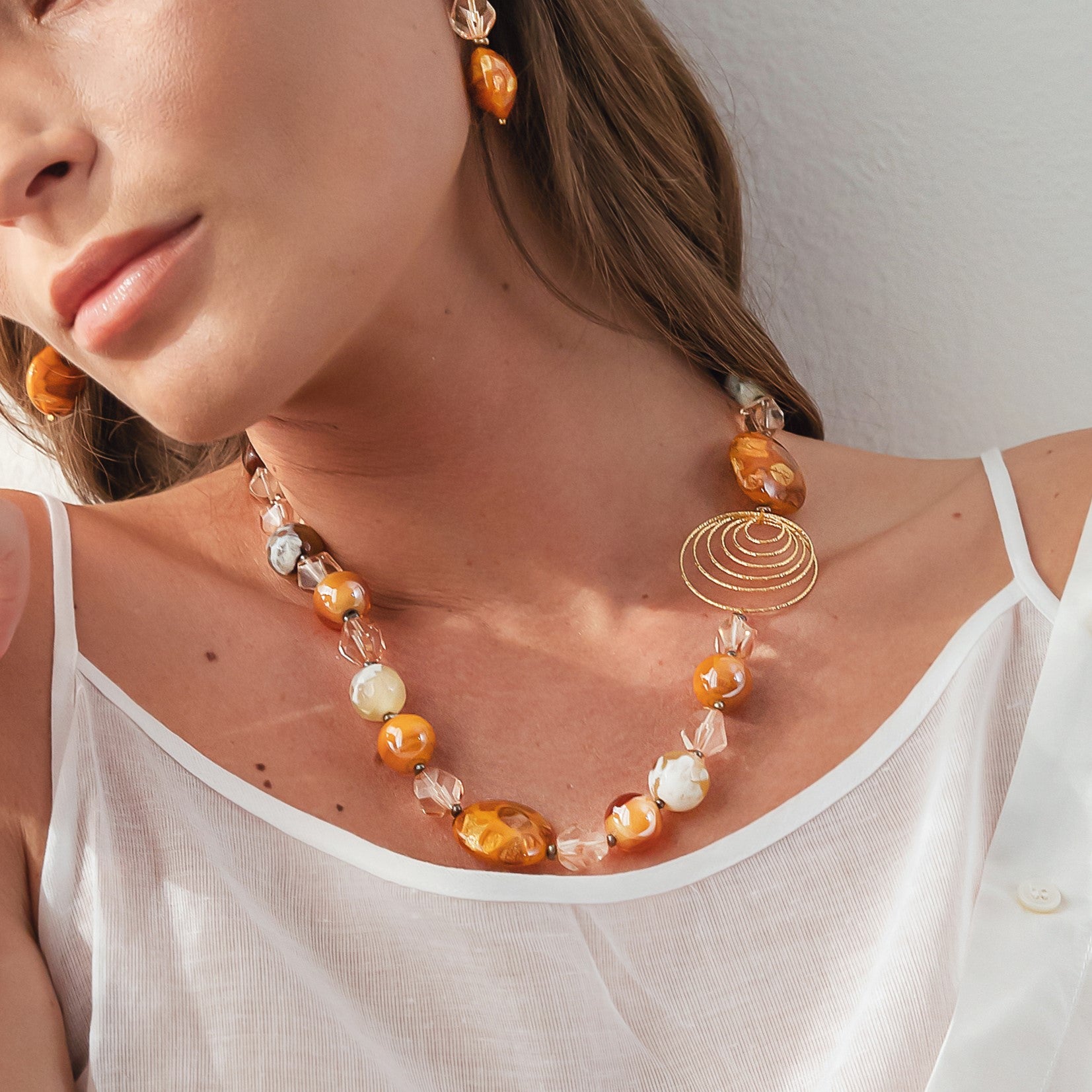 Model wearing MURRINAMURANO Venezia necklace and Earrings from the Aura Collection, handcrafted in Original Murano glass, 18KT Gold Finish or Rhodium finish, over Brass. Made in Italy – murrinamurano.us