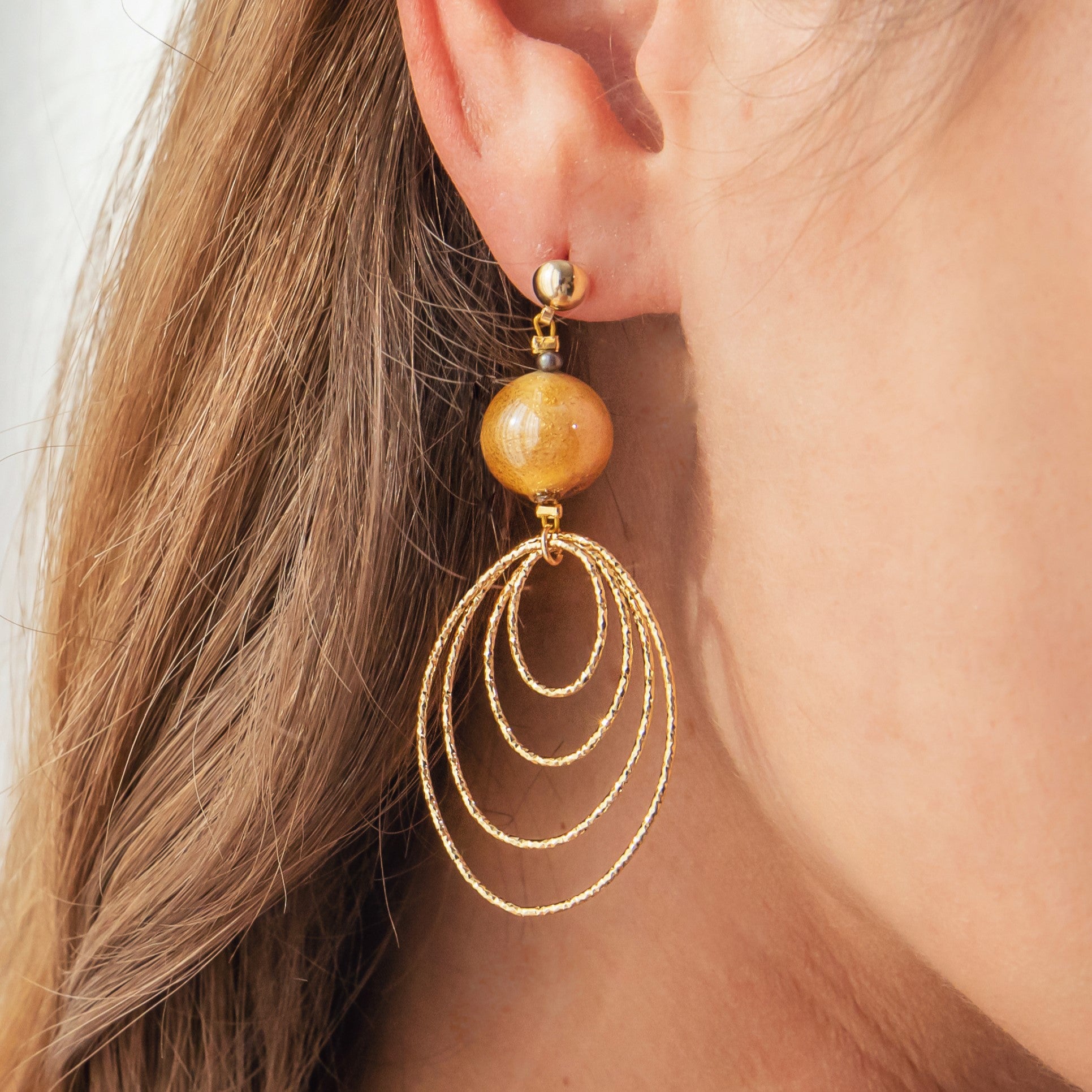 Model wearing MURRINAMURANO Venezia earrings from the Aura Collection, handcrafted in Original Murano glass, 18KT Gold Finish  over Brass. Made in Italy – murrinamurano.us