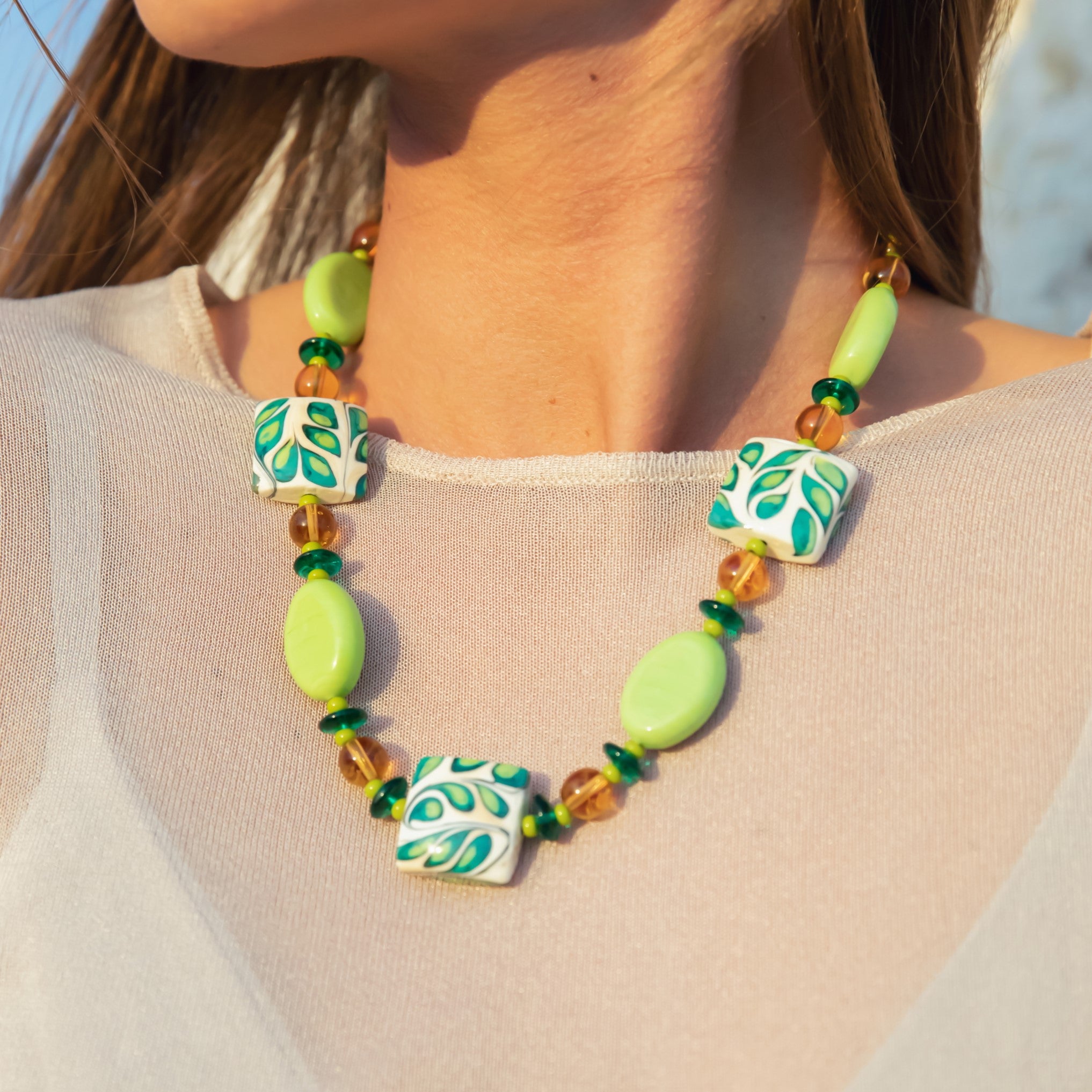 Model wearing MURRINAMURANO Venezia Necklace from the Coral Bay Collection, handcrafted in Original Murano glass, 18KT Gold Finish or Rhodium finish, over Brass. Made in Italy – murrinamurano.us
