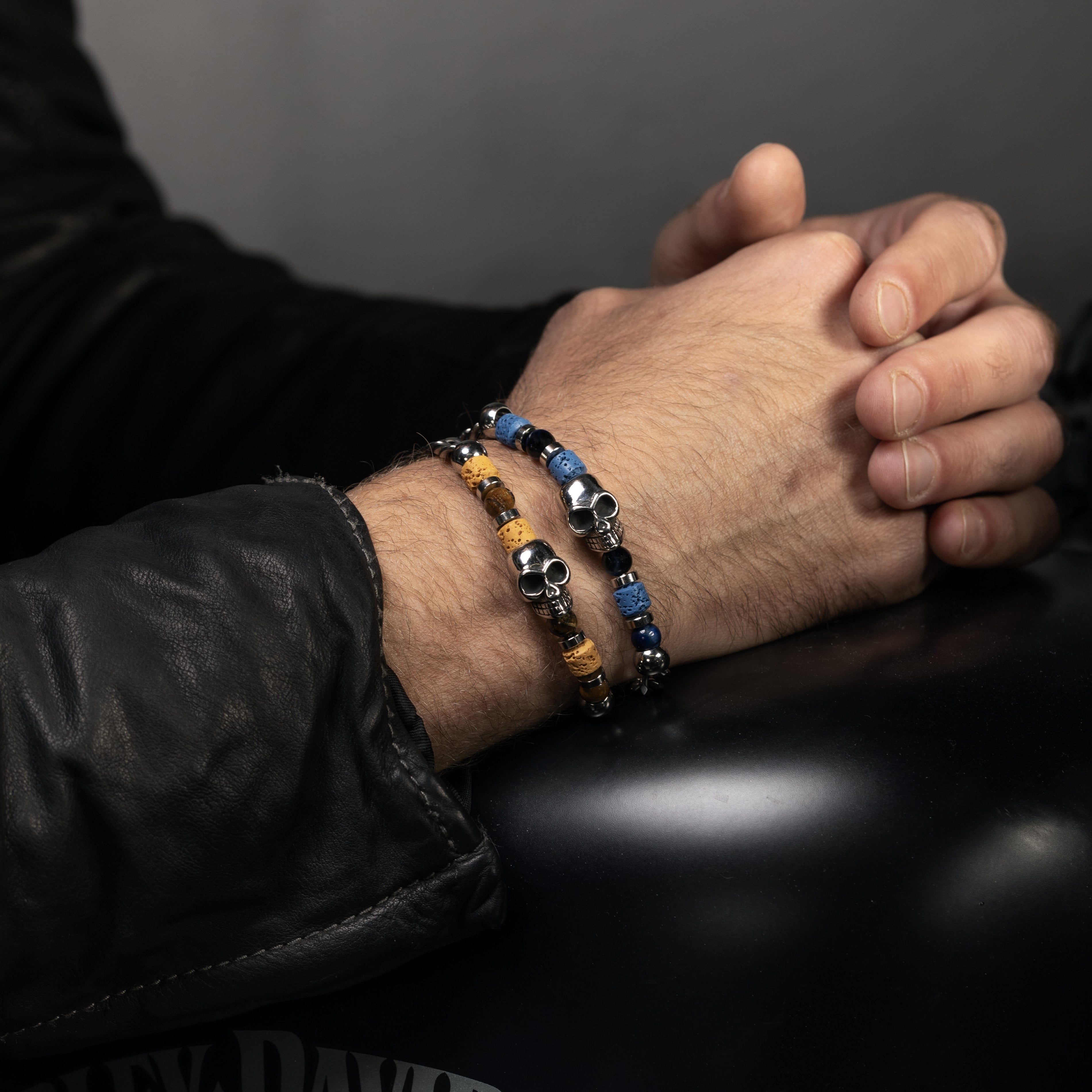 Hand wearing a Dusk Collection men’s bracelet with stainless steel chain, lava stone, tiger eye and jasper beads, skull detail, 20 cm length, contemporary Italian design.