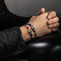 Hand wearing a Dusk Collection men’s bracelet with stainless steel chain, lava stone, tiger eye and jasper beads, skull detail, 20 cm length, contemporary Italian design.