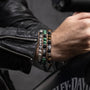 Close-up of a person's wrist wearing Batista men’s bracelet with tiger eye, malachite and glass beads, rhodium finish over stainless steel and brass, adjustable stretch fit, contemporary Italian design.