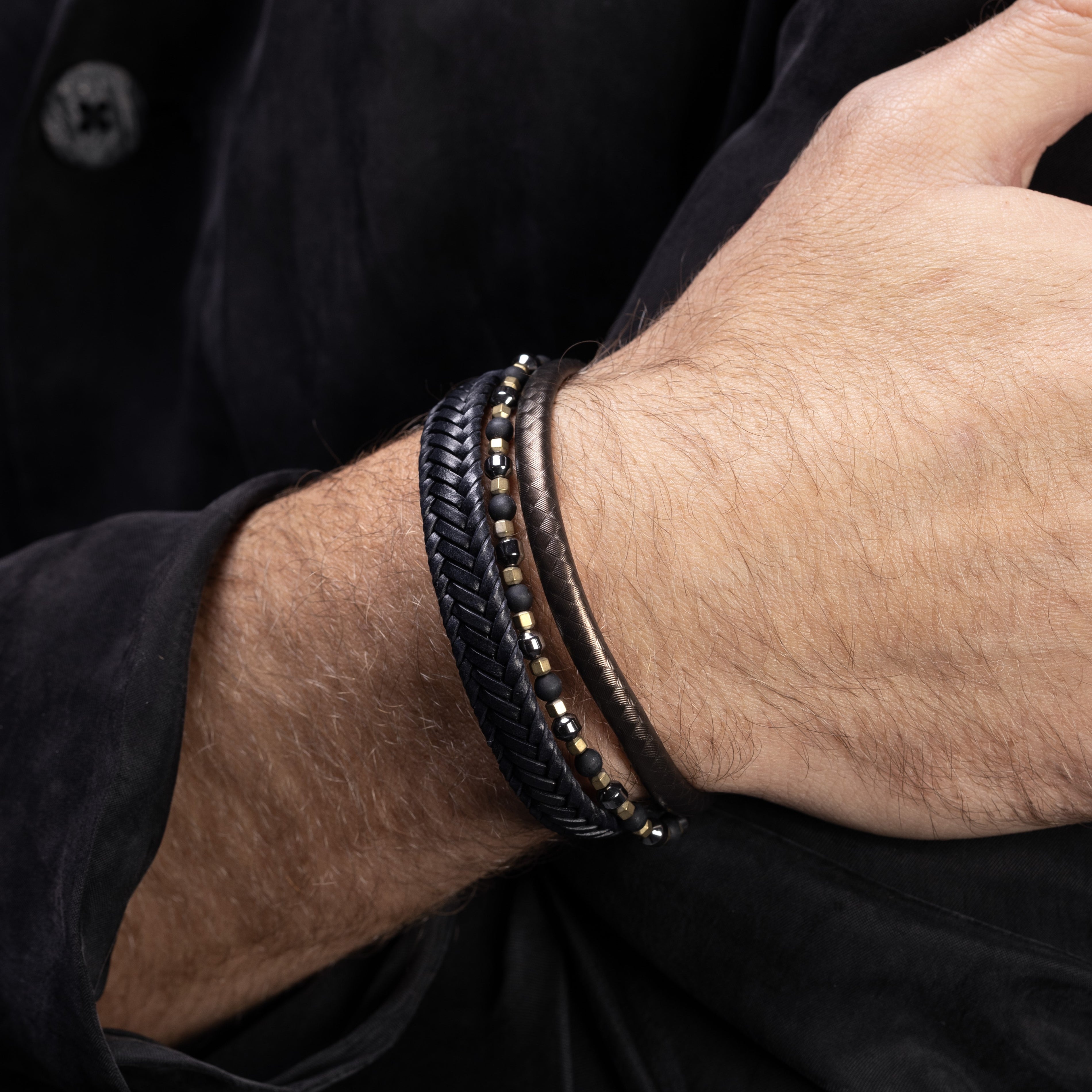 Close-up of a wrist wearing a Drip Collection men's bracelet with braided leather, hematite beads and stainless steel accents, 20 cm length, contemporary Italian men's jewelry.