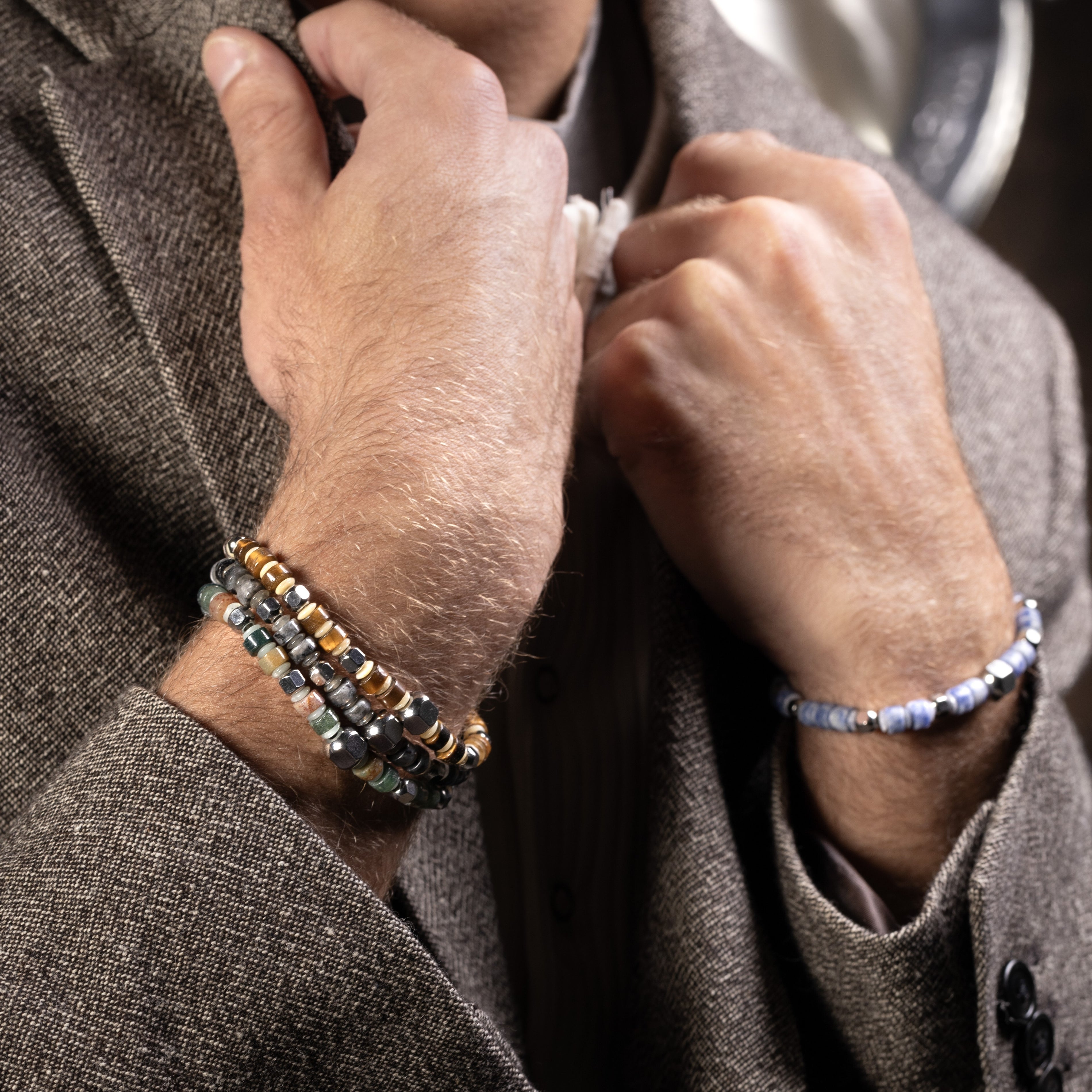 Close-up of hands wearing Blank men’s bracelet with jasper, lapis lazuli, labradorite and tiger eye stones, rhodium finish over stainless steel and brass, adjustable stretch fit, contemporary Italian design.