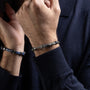 Close-up of a person wearing two Drift Collection men's bracelet with braided leather, stainless steel anchor detail and silicone accents, 21 cm length, contemporary Italian men's jewelry.