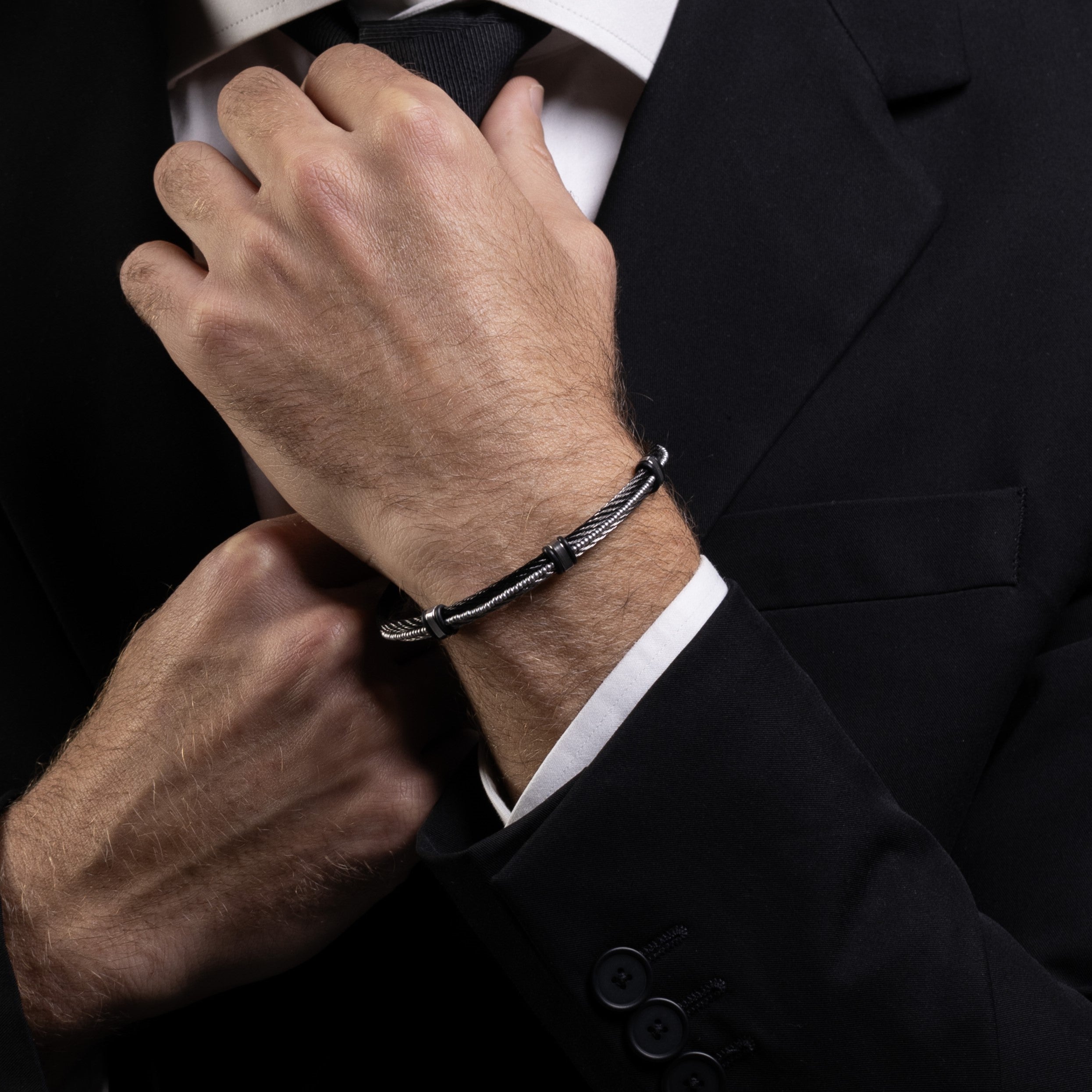 Spli Collection - Murano Glass, Person adjusting a tie with a black bracelet on a dark background