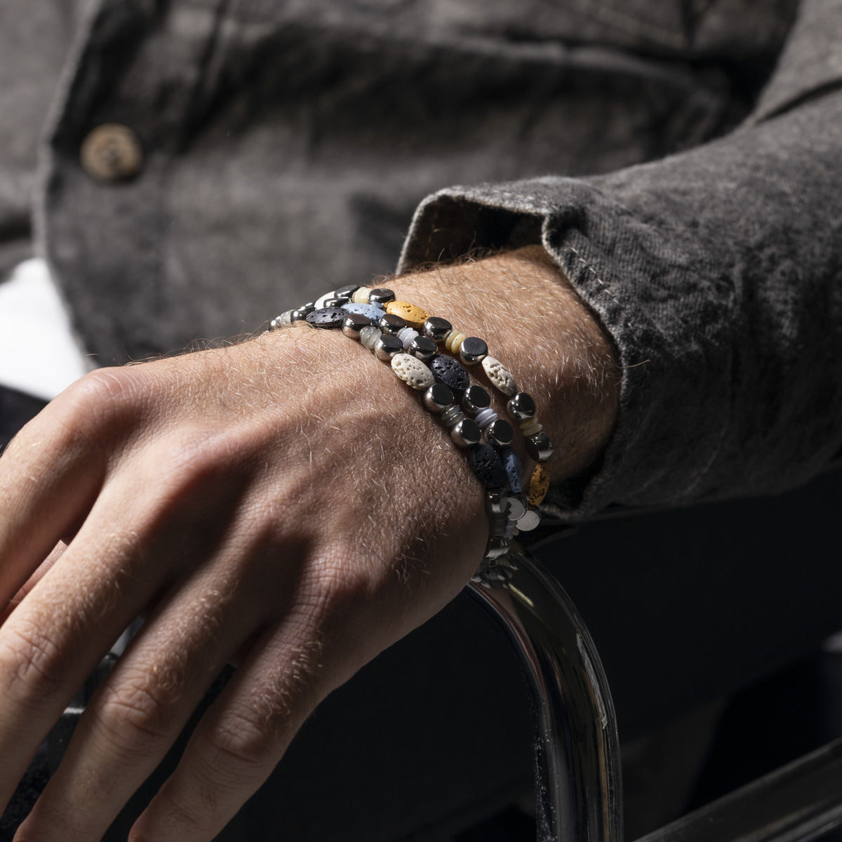 Close-up of a person's wrist wearing Hush Collection men’s bracelet with lava stone, stainless steel and brass, rhodium finish, 20 cm length.
