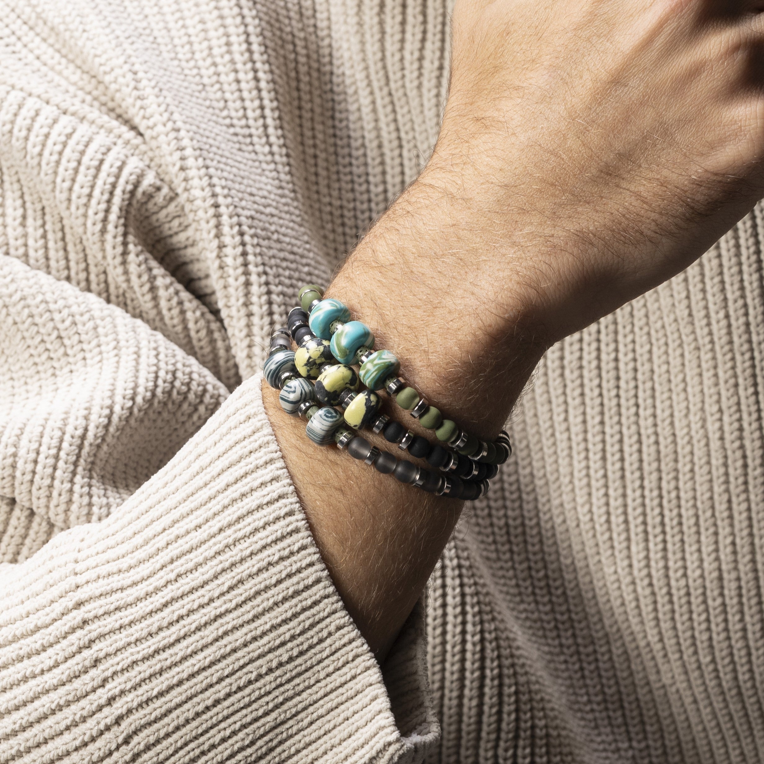Close-up of a wrist wearing multiple Burn men’s bracelet with ceramic, lava stone and steel elements, rhodium finish over stainless steel and brass, adjustable fit, contemporary Italian design.