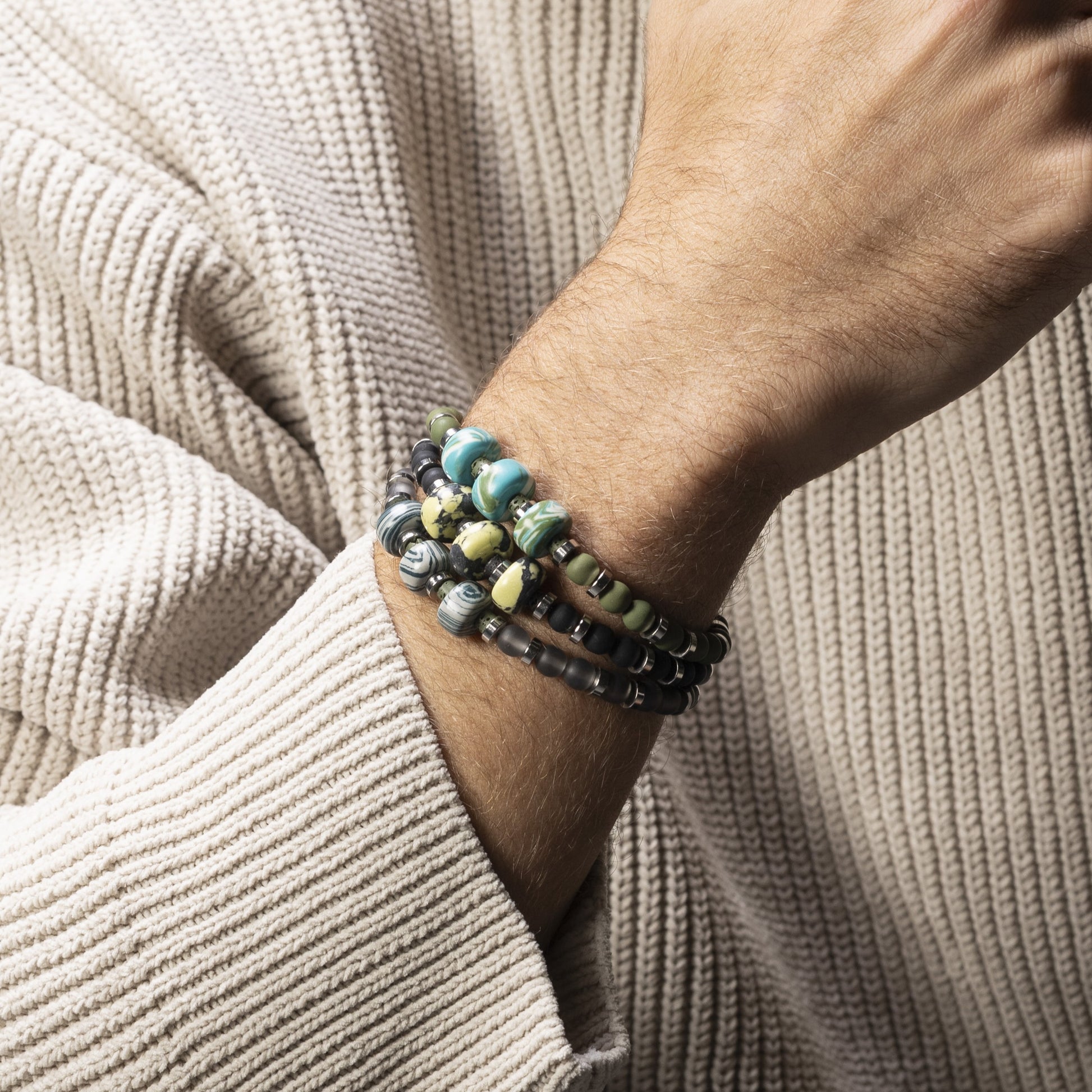 Close-up of a wrist wearing multiple Burn men’s bracelet with ceramic, lava stone and steel elements, rhodium finish over stainless steel and brass, adjustable fit, contemporary Italian design.