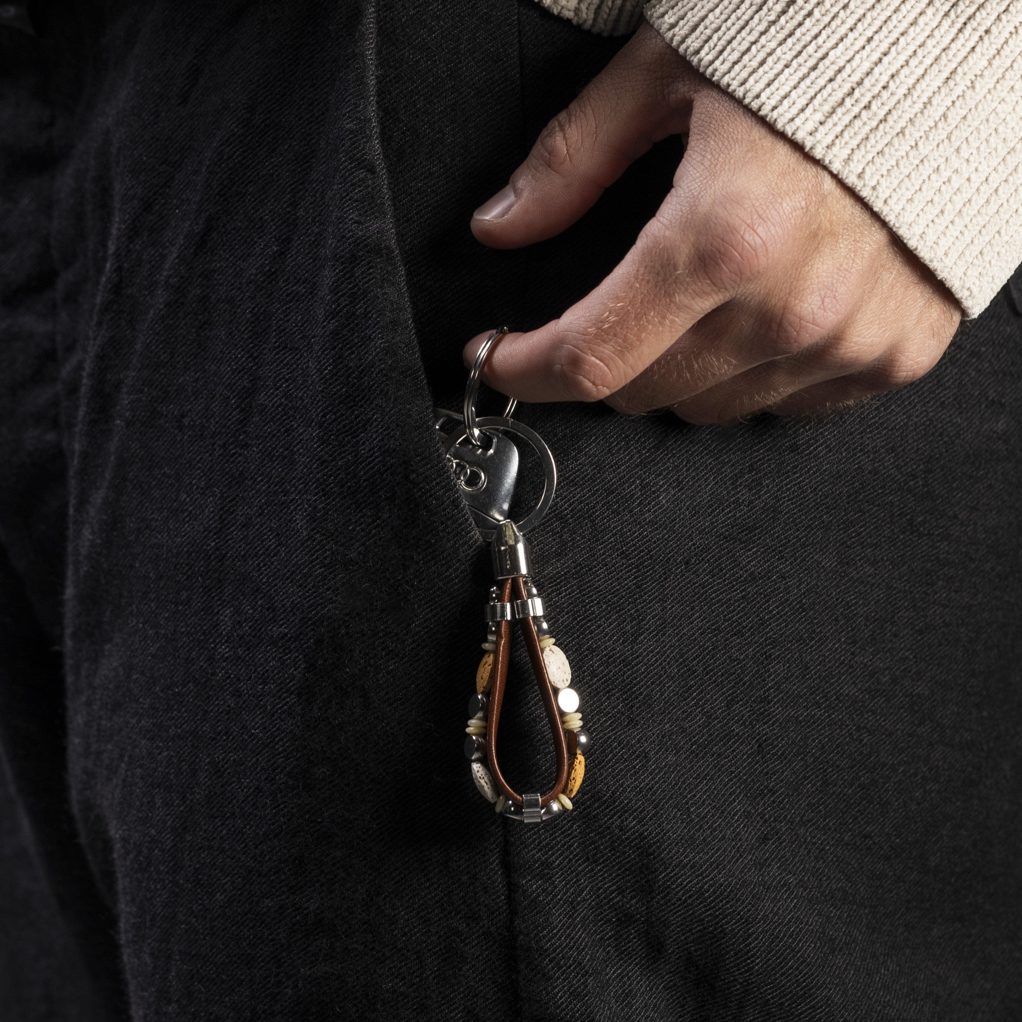 Person holding a Hush Collection men’s keychain with leather, lava stone, stainless steel and brass, rhodium finish, 10 cm length.