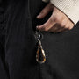 Person holding a Hush Collection men’s keychain with leather, lava stone, stainless steel and brass, rhodium finish, 10 cm length.