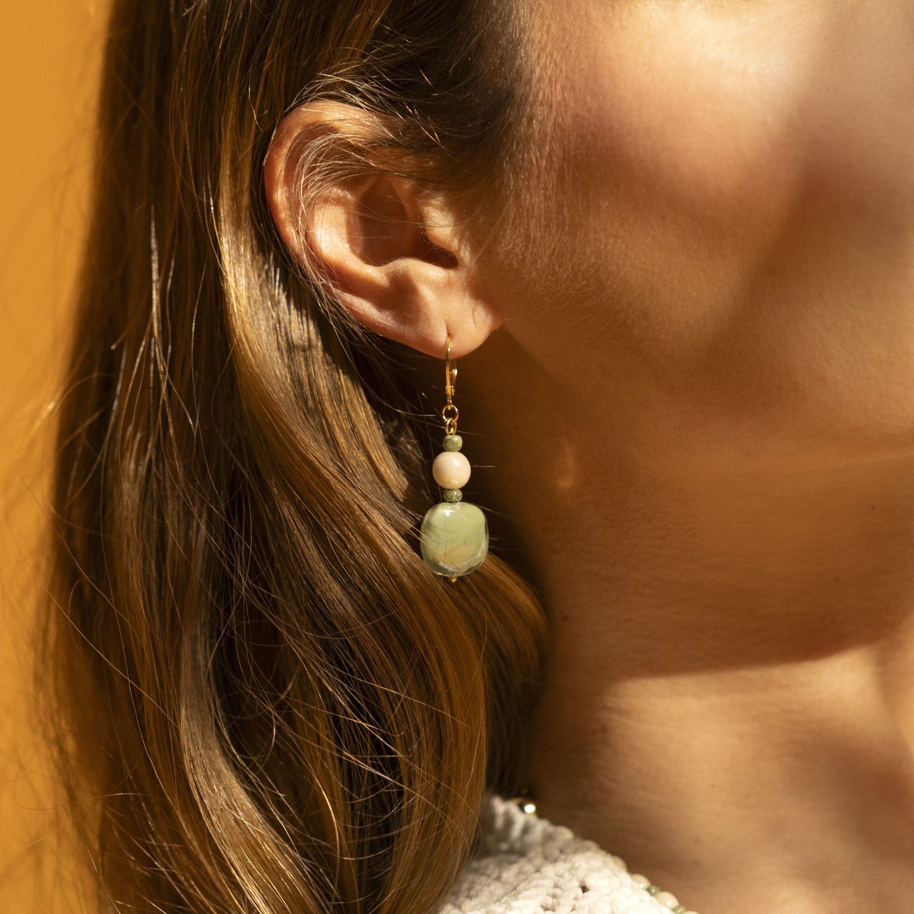 Bloom Murano glass drop earrings with carnelian stone and brass components, 18KT Gold Finish, 2 inches, handcrafted in Venice, Italy. Close-up of an ear wearing a green beaded earring with a blurred background