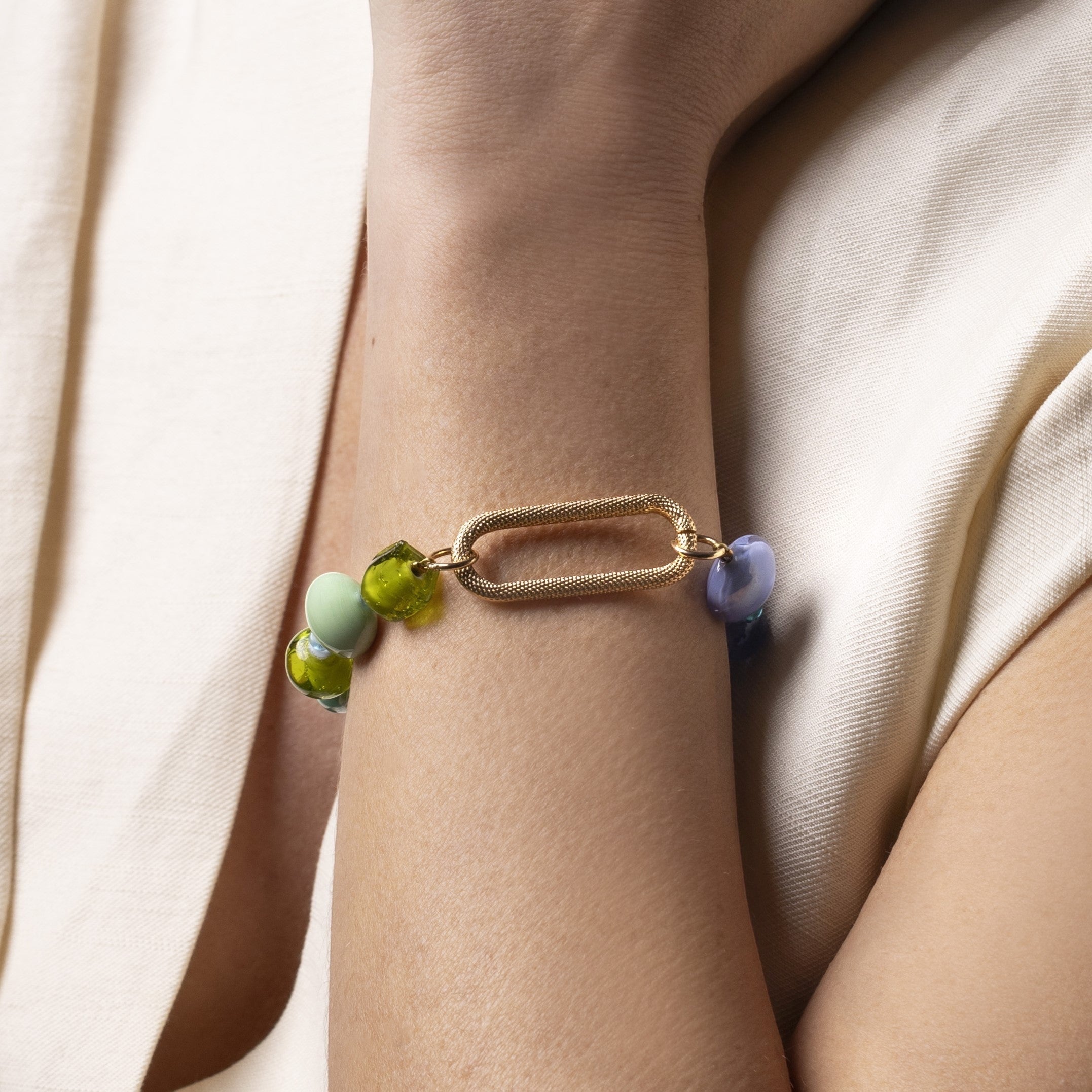 Breeze Murano glass link bracelet with 18KT Gold Finish over brass, steel and aluminum components, adjustable 7 inches with extension, handcrafted in Venice, Italy. on a wrist against a beige background