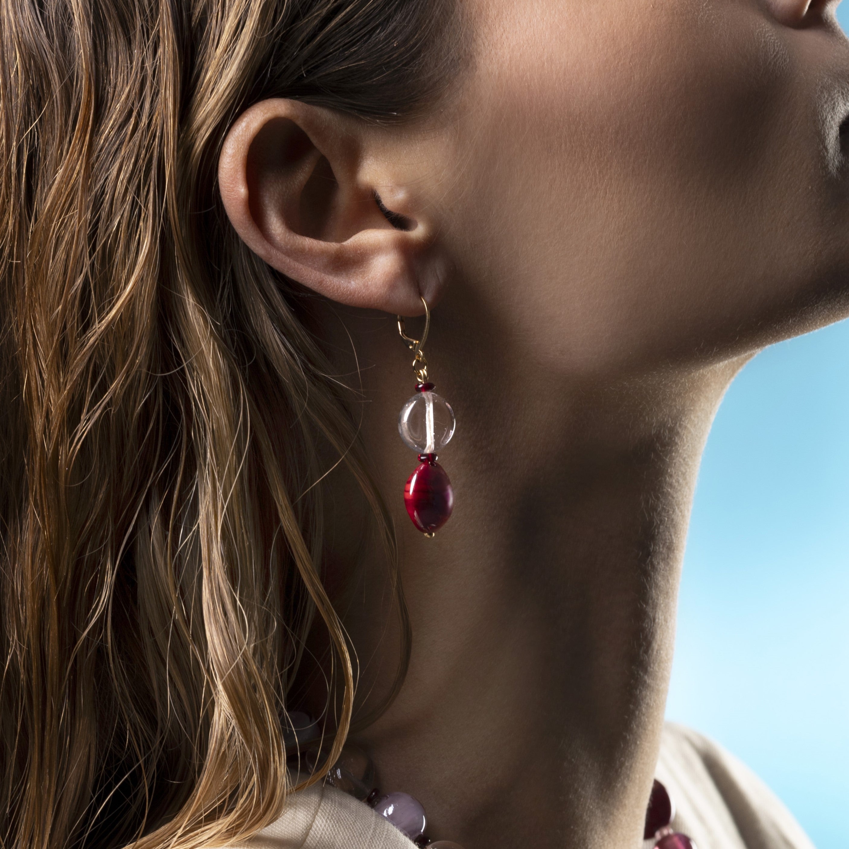 Close-up of a person wearing a Breeze Murano glass drop earrings with 18KT Gold Finish over brass, 2 inches long, handcrafted in Venice, Italy.