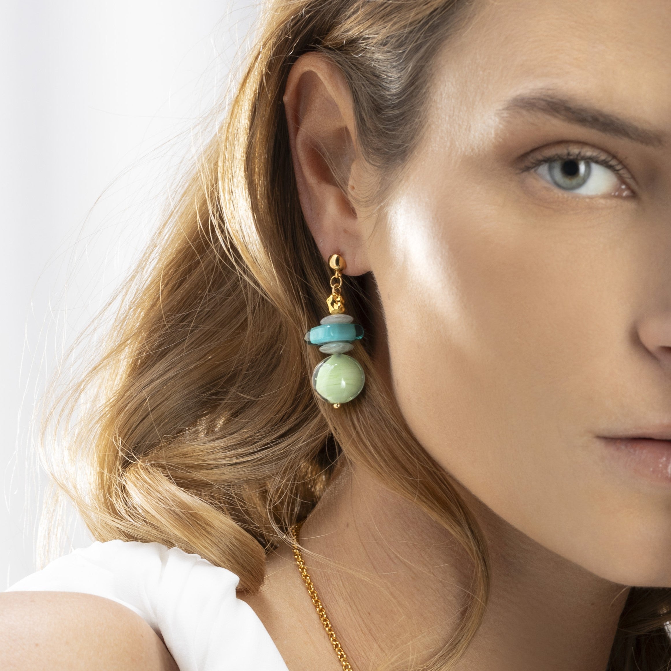 Evoque Collection - Murano Glass - Close-up of a woman wearing gold and turquoise earrings with a neutral background