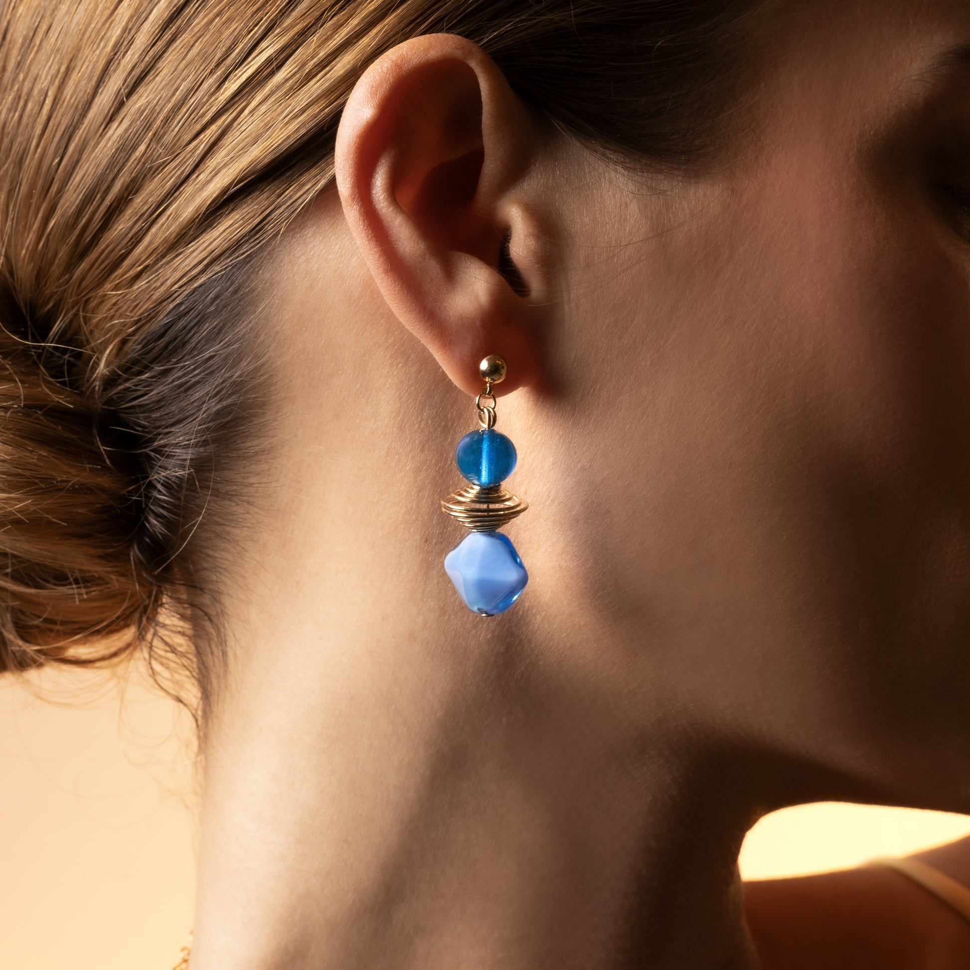 Close-up of a woman wearing a Glow Murano glass drop earrings with 18KT Gold Finish over brass, handcrafted in Venice, Italy, 2 inches length.