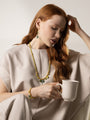 Veil Long Necklace with green Murano Glass beads, 18K Gold-finished metal details, and hard stone accents worn with a cream outfit. MurrinaMurano.us