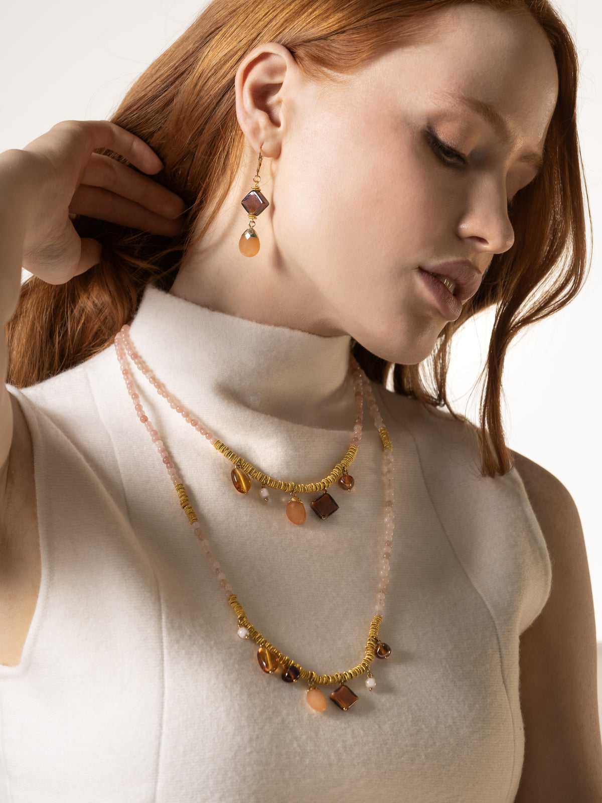 Veil Long Necklace with pale pink Murano Glass beads, 18K Gold-finished metal details, and hard stone accents worn with a cream outfit.