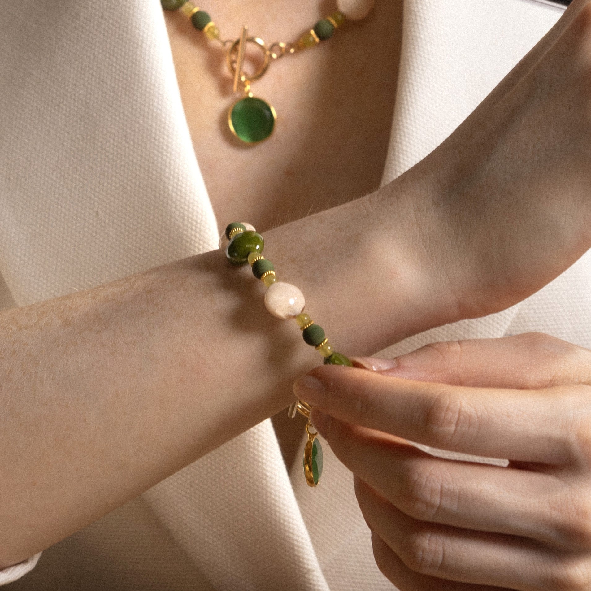 MurrinaMurano.us model wearing the green Trace Bracelet, featuring rounded Murano Glass beads, pale stone accents, and a faceted green glass pendant with gold-finished details. Handcrafted in Italy.