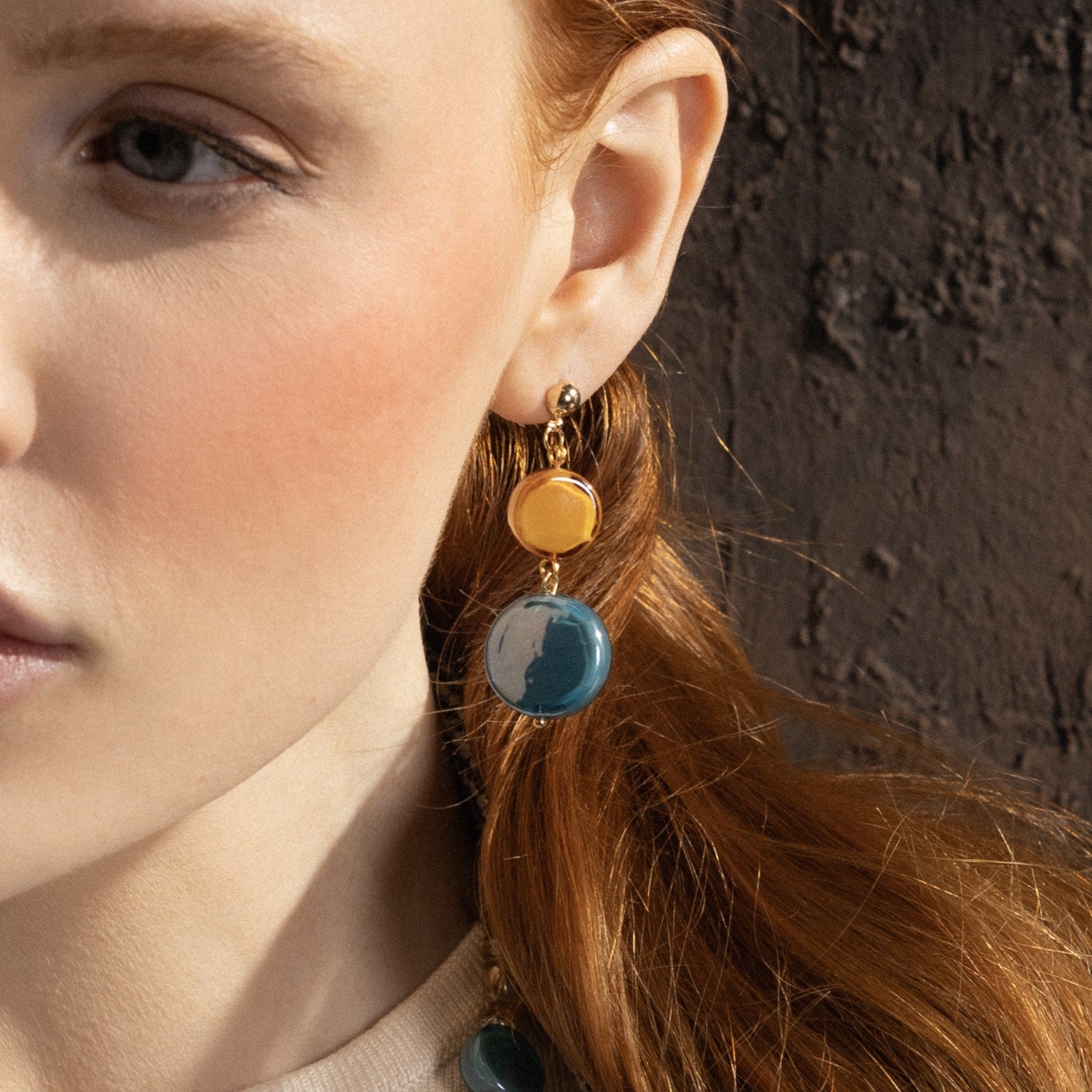 Woman wearing Edge Murano glass drop earrings with blue and orange glass elements, 18K gold finish over brass, handcrafted in Italy.