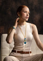 Woman wearing an Edge Murano glass pendant necklace with layered glass elements and faceted teardrop pendant, 18KT Gold Finish over brass, handcrafted in Italy.