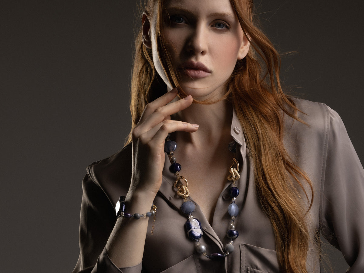 Model wearing the Frame Bracelet in cool blue Murano Glass with purple accents and sculptural gold-finished elements, shown against a dark outfit. Handcrafted in Italy.