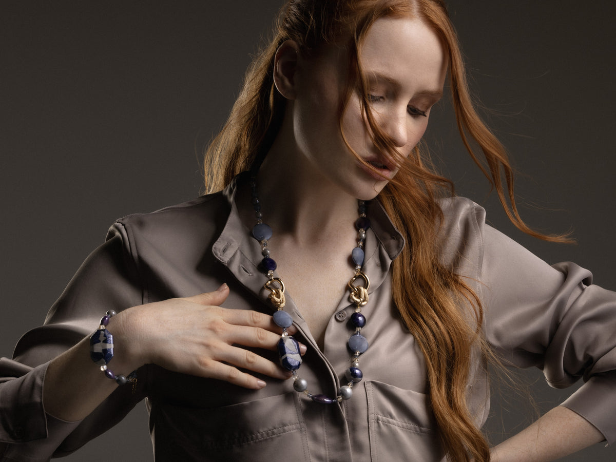 Close view of a woman wearing the blue Frame Murano Glass Bracelet, highlighting the layered glass beads, polished metal accents, and architectural centerpiece. Handcrafted in Italy.