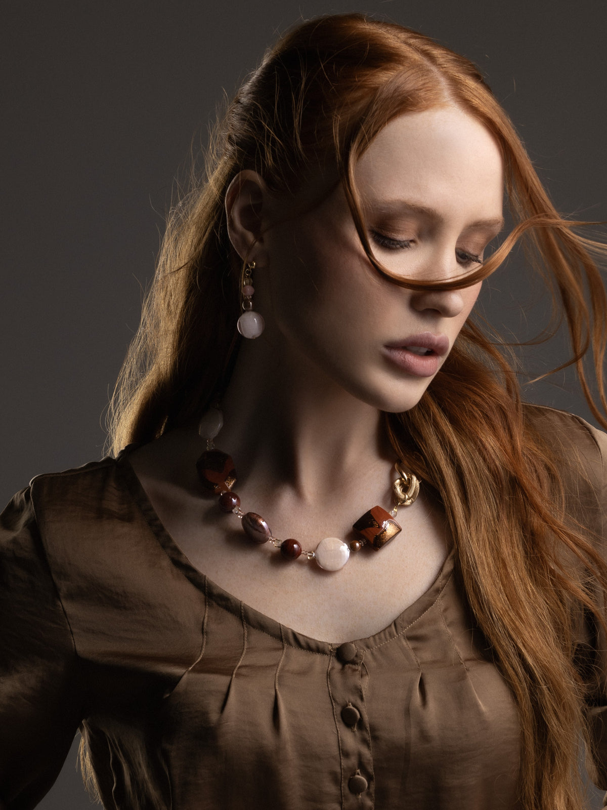 MurrinaMurano.us Frame drop earrings in brown Murano Glass styled on a model, with warm amber and chocolate-toned glass accents creating a soft contrast against her dark outfit. Handcrafted in Italy.