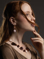 Side view of a model wearing MurrinaMurano.us Frame drop earrings, featuring translucent brown Murano Glass beads and large rounded glass pendants with gold-finished details. Handcrafted in Italy.
