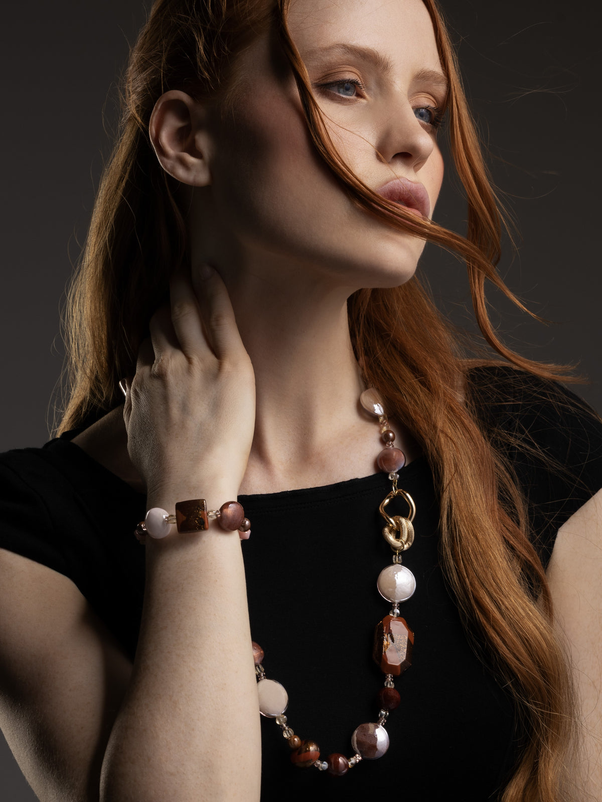 Model wearing the brown Frame Opera Necklace, with amber and smoky Murano Glass elements arranged along an elongated silhouette and sculptural gold-finished links. Handcrafted in Italy.