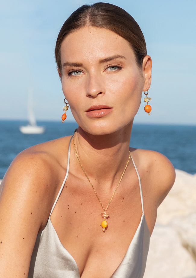 Model wearing MURRINAMURANO Venezia earrings and necklace from the Ocean Odyssey Collection, handcrafted in Original Murano glass, 18KT Gold Finish or Rhodium finish, over Brass. Made in Italy – murrinamurano.us
