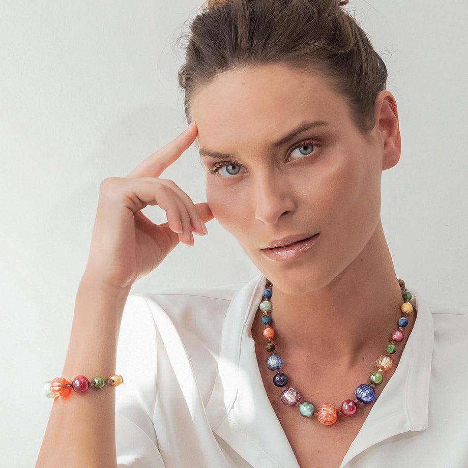 Model wearing MURRINAMURANO Venezia necklace  and bracelet from the Gea Collection, handcrafted in Original Murano glass, 18KT Gold Finish or Rhodium finish, over Brass. Made in Italy – murrinamurano.us